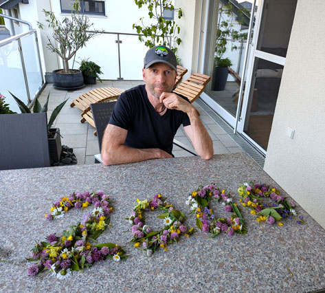 Foto Mann sitzt auf einem Balkon, vor ihm auf dem Tisch ist die Zahl 2000 in Blumen ausgelegt
