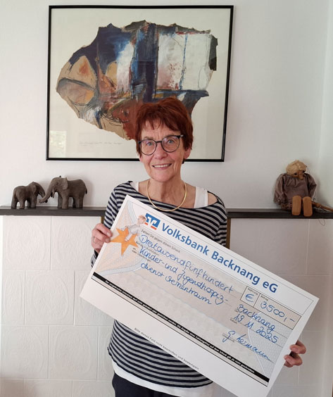 Hermann, Gabi Das Bild zeigt eine Frau mittleren Alters, die lächelnd in die Kamera schaut und einen übergroßen Scheck der Volksbank Backnang eG mit einer Spende von 3500 Euro hält. Der Scheck ist für den