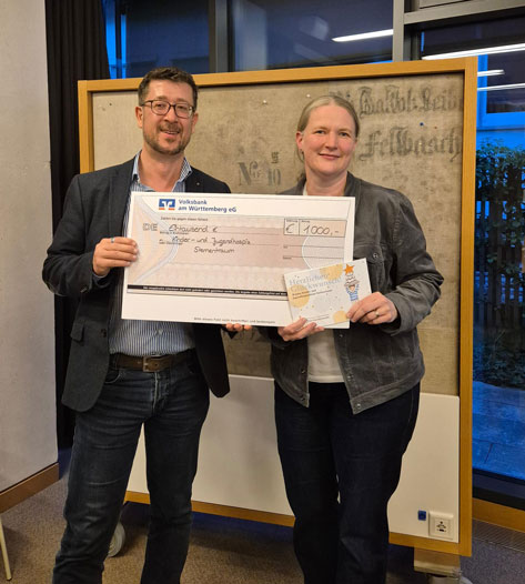 Ein Mann und eine Frau präsentieren einen Scheck über 1000 Euro und eine Grußkarte.