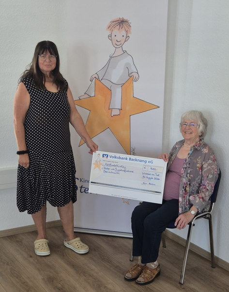 Spende Maria Hinderer Zwei Frauen halten einen Scheck, der Volksbank Backnang eG, über 850 Euro. Im Hintergrund ist ein Banner mit einem gezeichneten Sternenkind zu sehen.